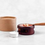 Aquecedor manual com uma vela branca e uma caixa castanha
