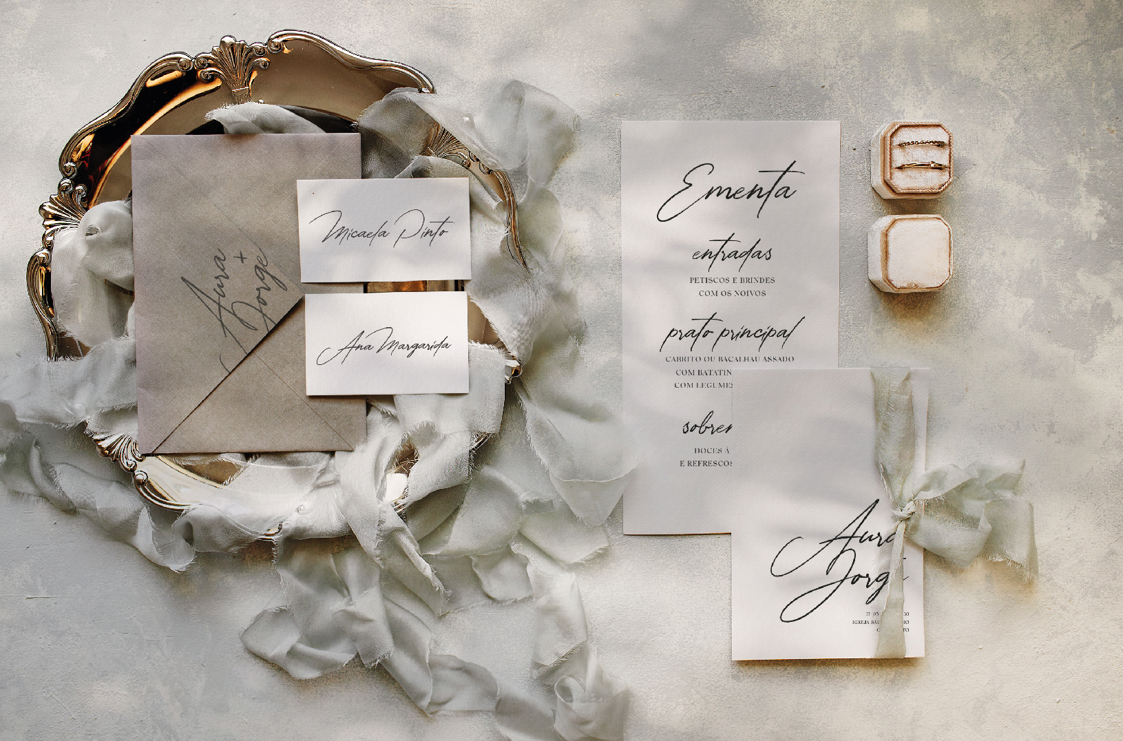 Ementa, marcador de lugar e convite de casamento de estilo tipográfico com um laço de linho bege, com um envelope cinza pousado numa bandeja dourada