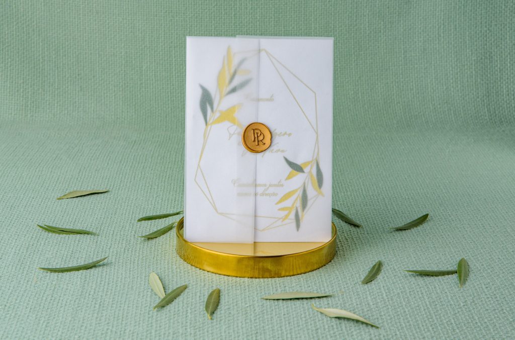 Convite de casamento com detalhes florais e detalhes em dourado e envelope em papel vegetal com lacre dourado em base dourada