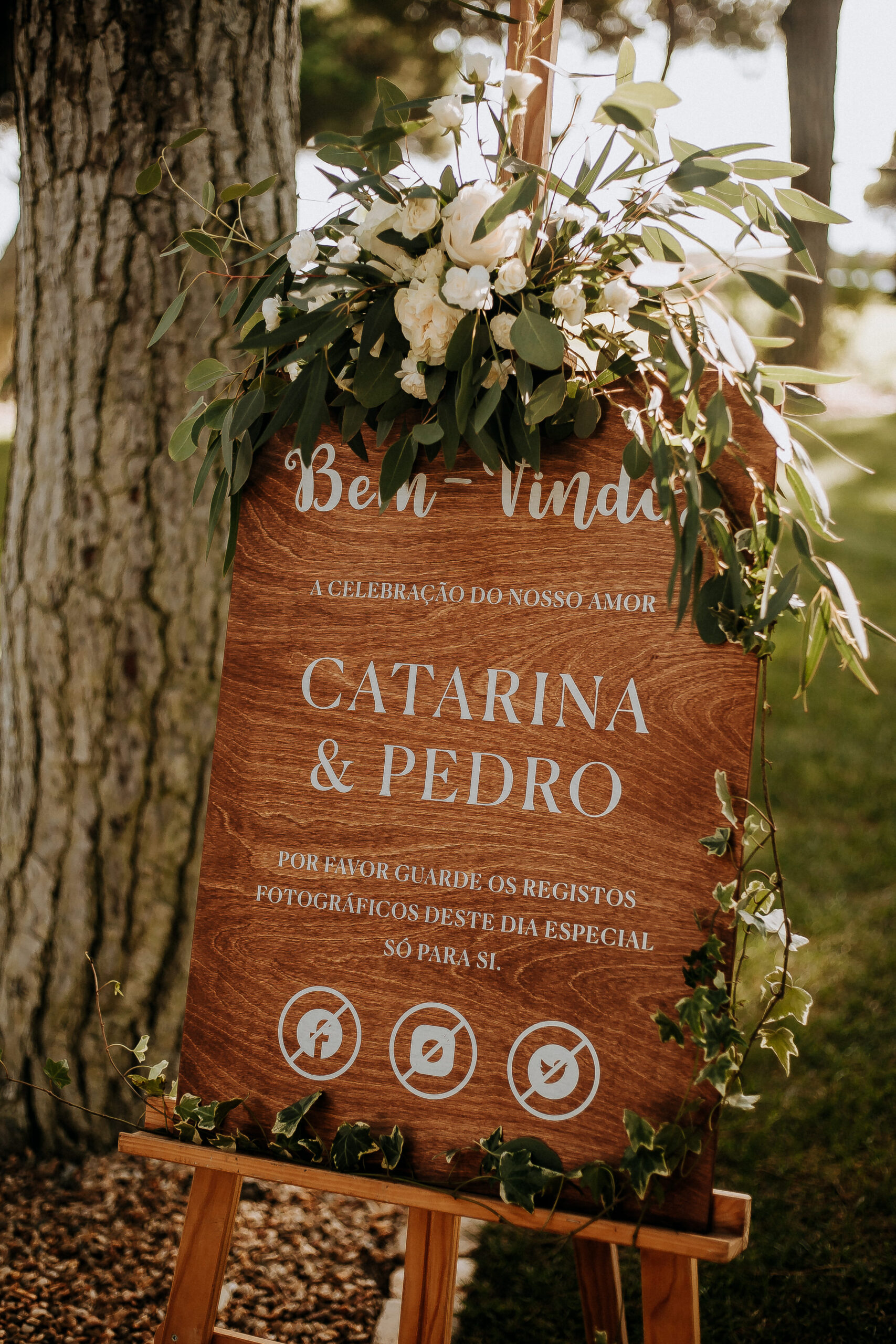 Placa de boas vindas em madeira com apontamentos decorativos florais num cavalete de madeira