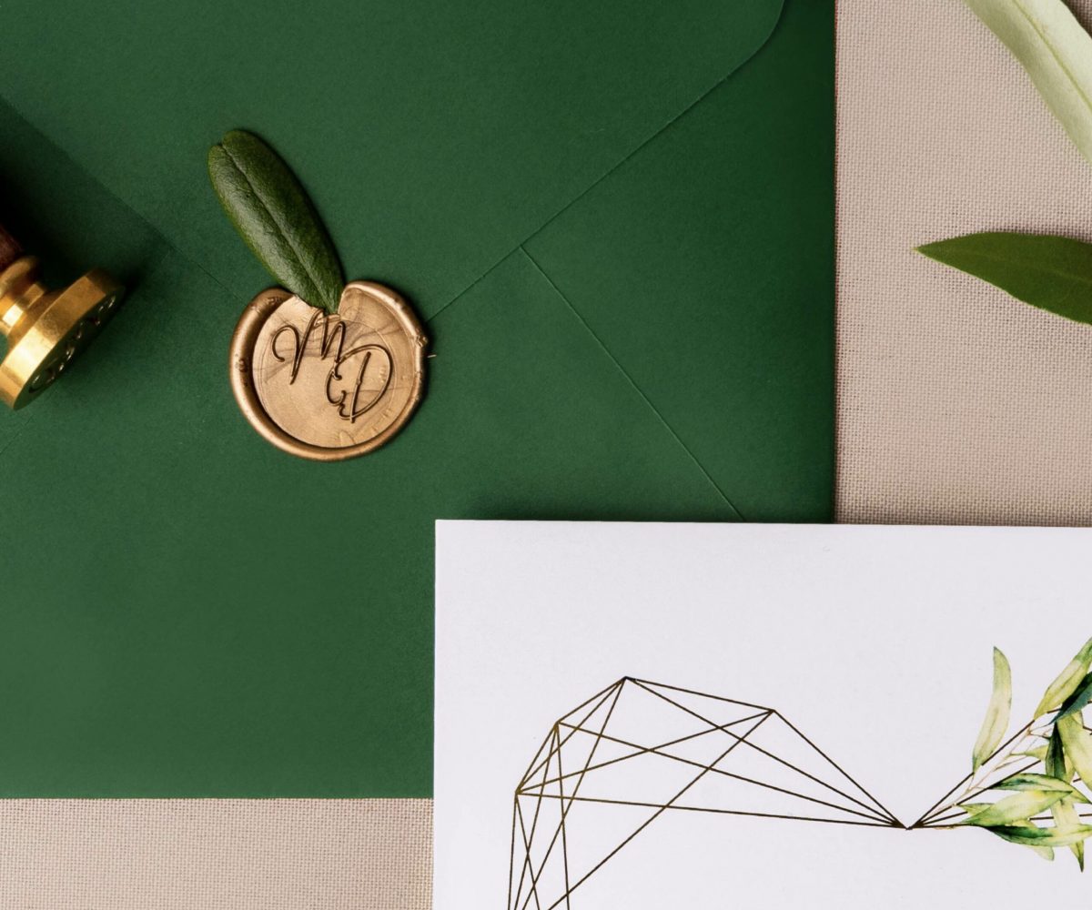 Convite de casamento com foil dourado, apontamentos naturais e envelope verde, selado com lacre dourado.